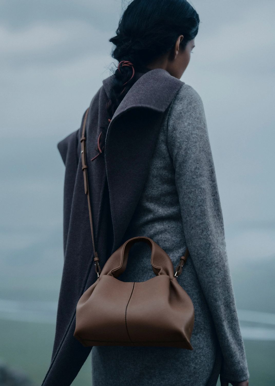 Person wearing a gray coat and carrying a Polène Numéro Neuf Mini Edition Textured Root on a foggy day.