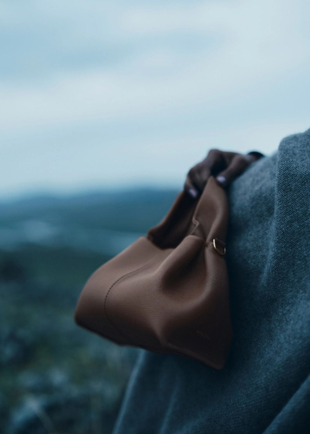 Polène Numéro Neuf Mini Edition Textured Root draped over a shoulder with a blurred natural background