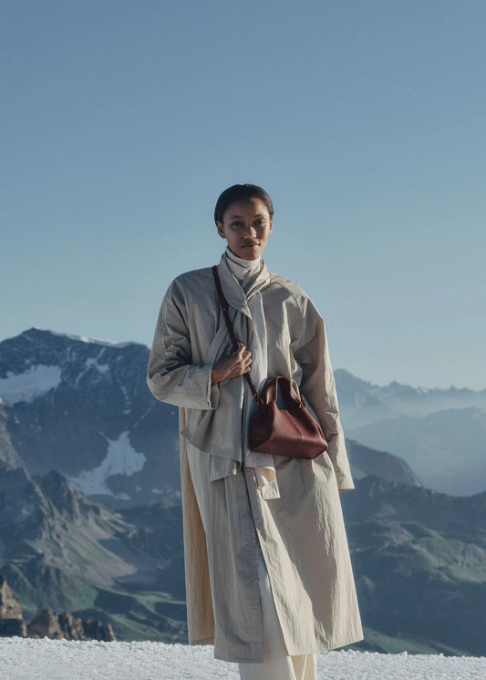 Person wearing Polène Numéro Neuf Mini Edition Textured Black Cherry standing on a snowy mountain with a clear blue sky