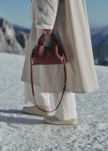 Person holding a Polène Numéro Neuf Mini Edition Textured Black Cherry in a snowy landscape with mountains in the background