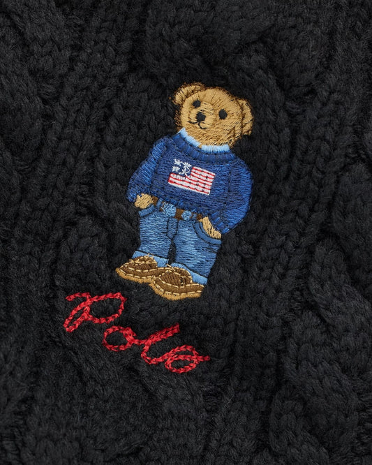 Embroidered teddy bear with a blue sweater and American flag design on a textured black fabric background.
