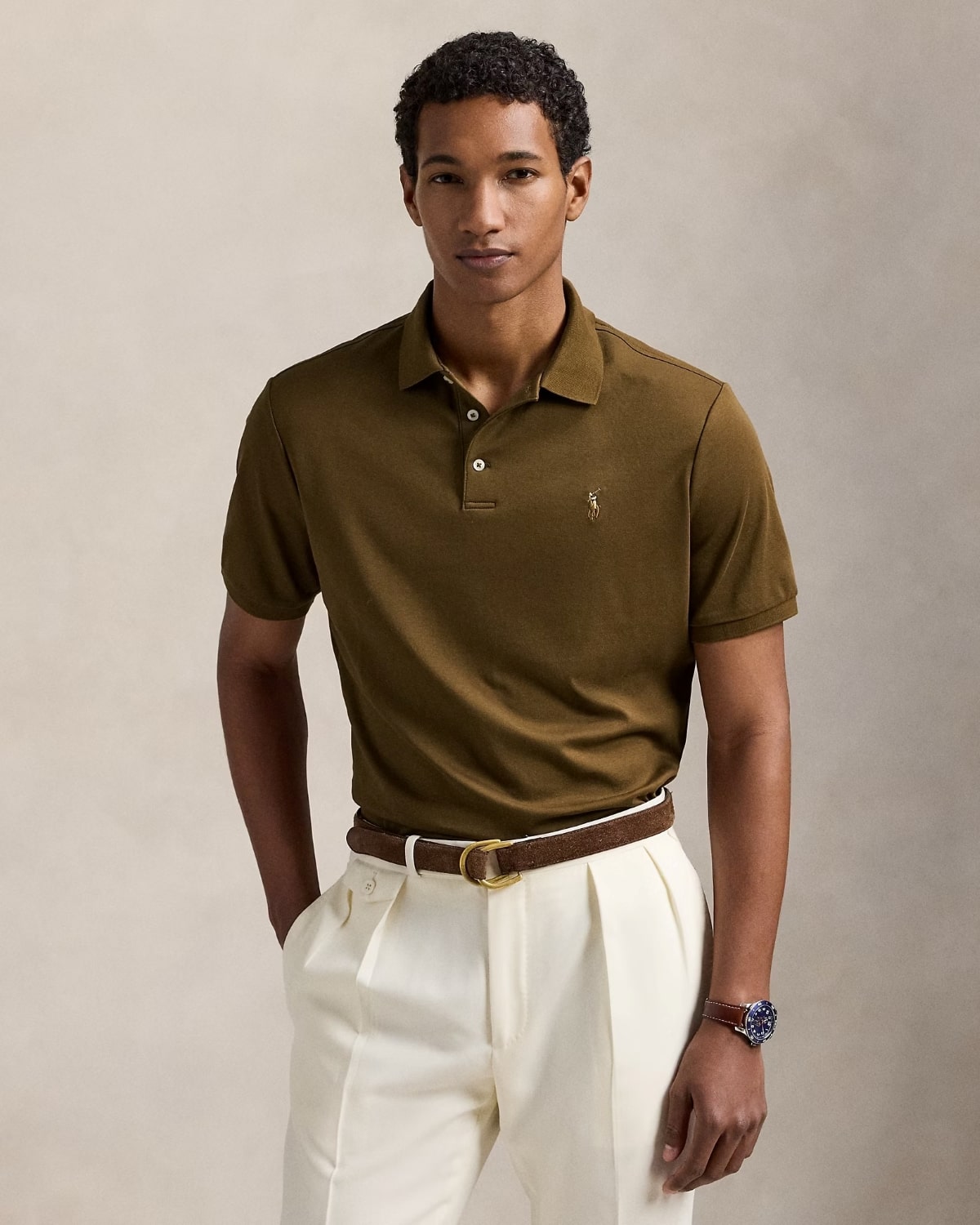 Man wearing a Polo Ralph Lauren Men’s Soft Cotton Polo Shirt Classic Fit – Nature Brown 710660606205 and white pants against a beige background