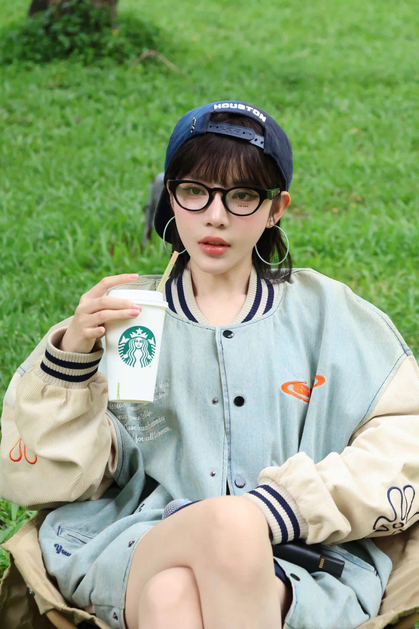 Women wearing Prada PR A11VD 16K1O1 Oval Black Eyeglasses holding a Starbucks cup outdoors on grass