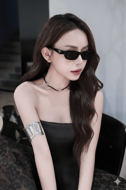 Woman wearing Prada PR B06S 16K08Z Square Symbole Sunglasses and a black dress with a blurred background
