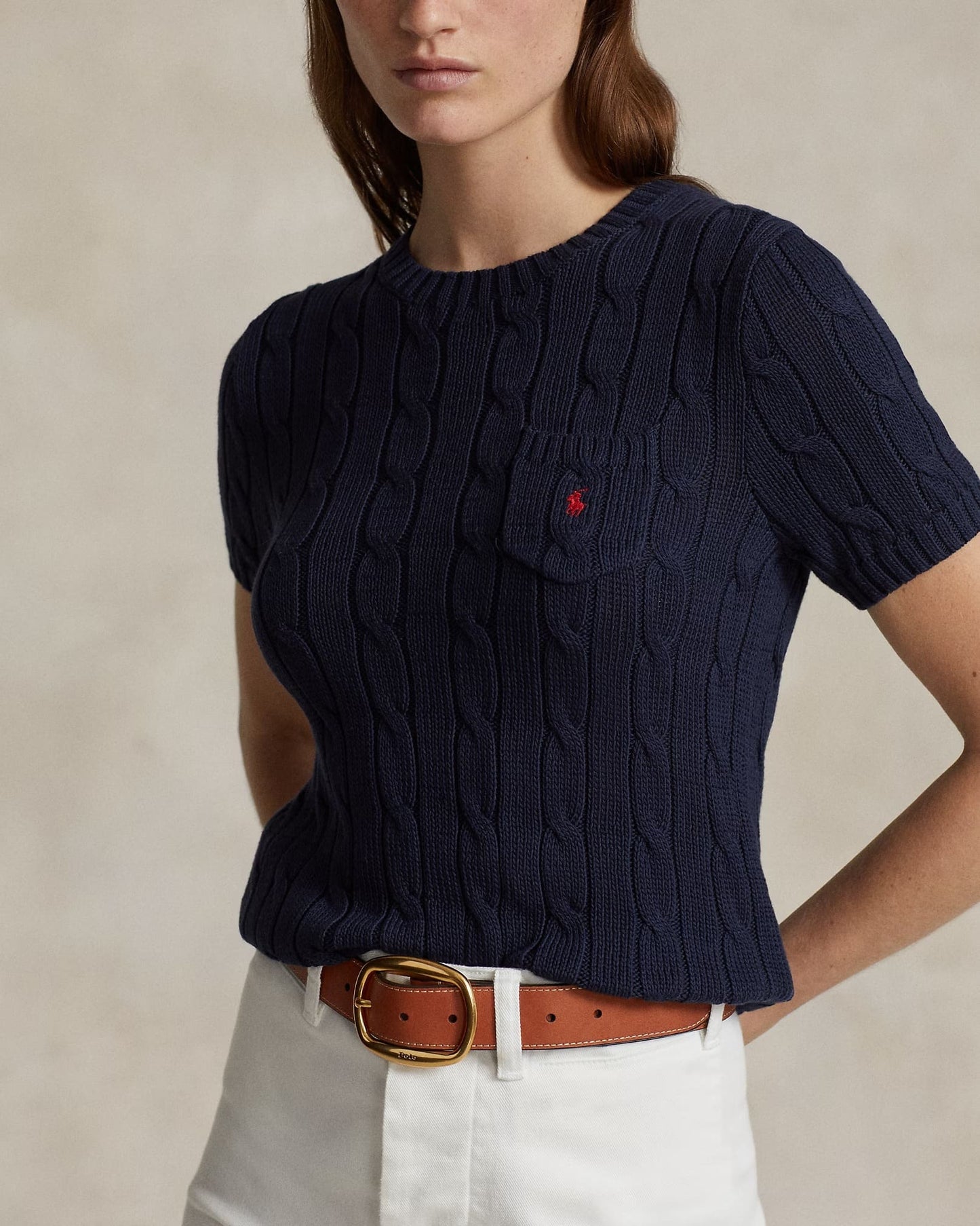 Navy blue cable knit sweater with a red logo on a beige background
