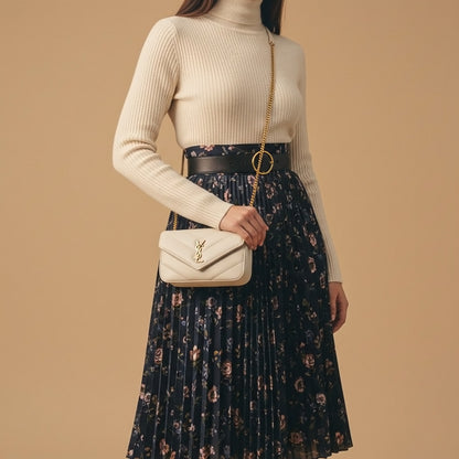 Person wearing a beige sweater and floral skirt, holding a Saint Laurent LOULOU MINI in Lambskin Blanc Vintage 821749AAEAX9207 with a brand logo on a beige background