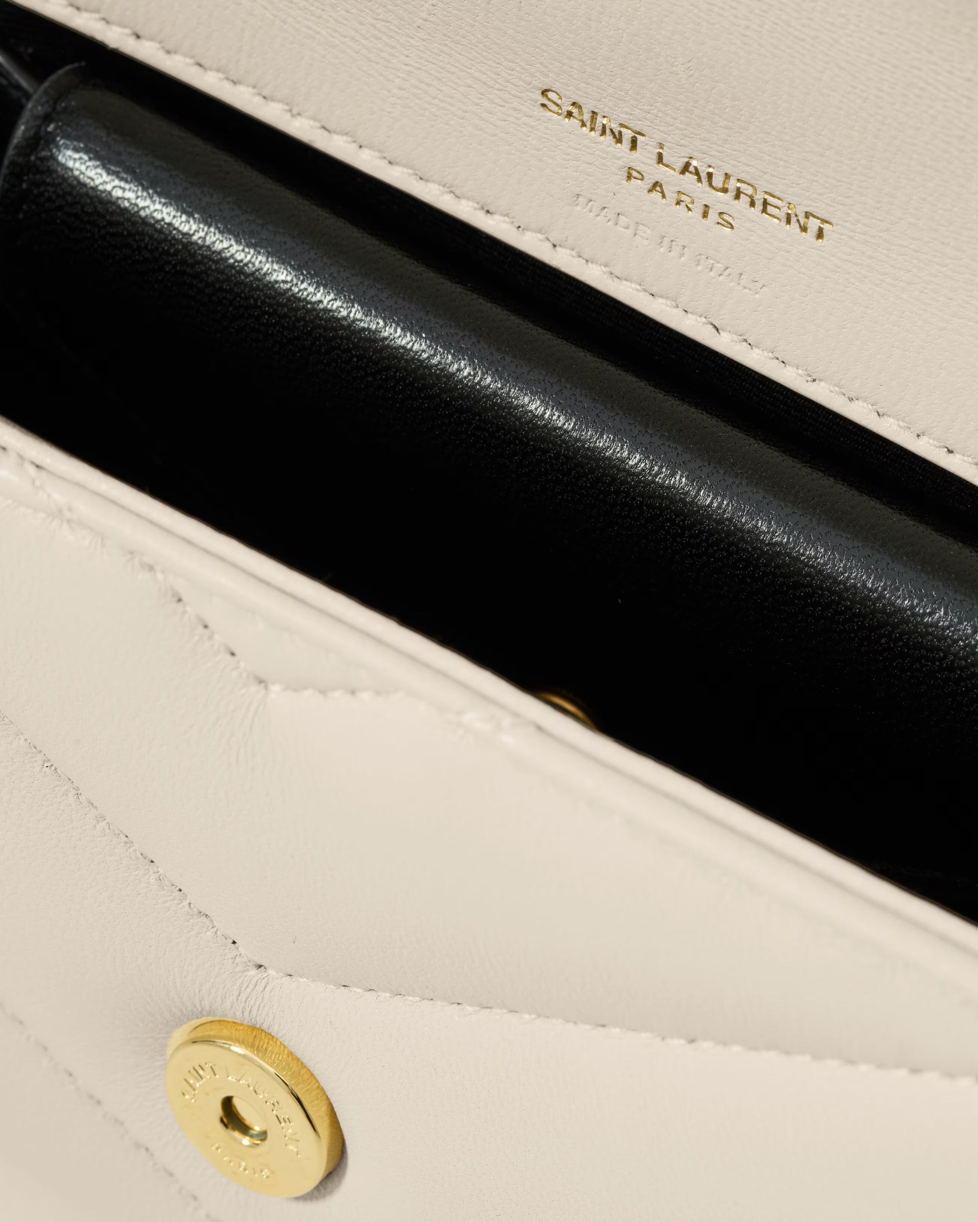 Close-up of a Saint Laurent handbag with gold logo and black interior.
