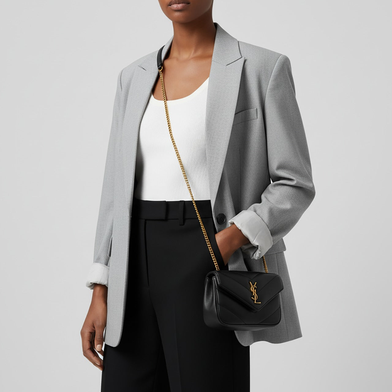 Person wearing a gray blazer, white top, and black pants with a Saint Laurent LOULOU MINI in Lambskin Black 821749AAEAX1000 on a light gray background