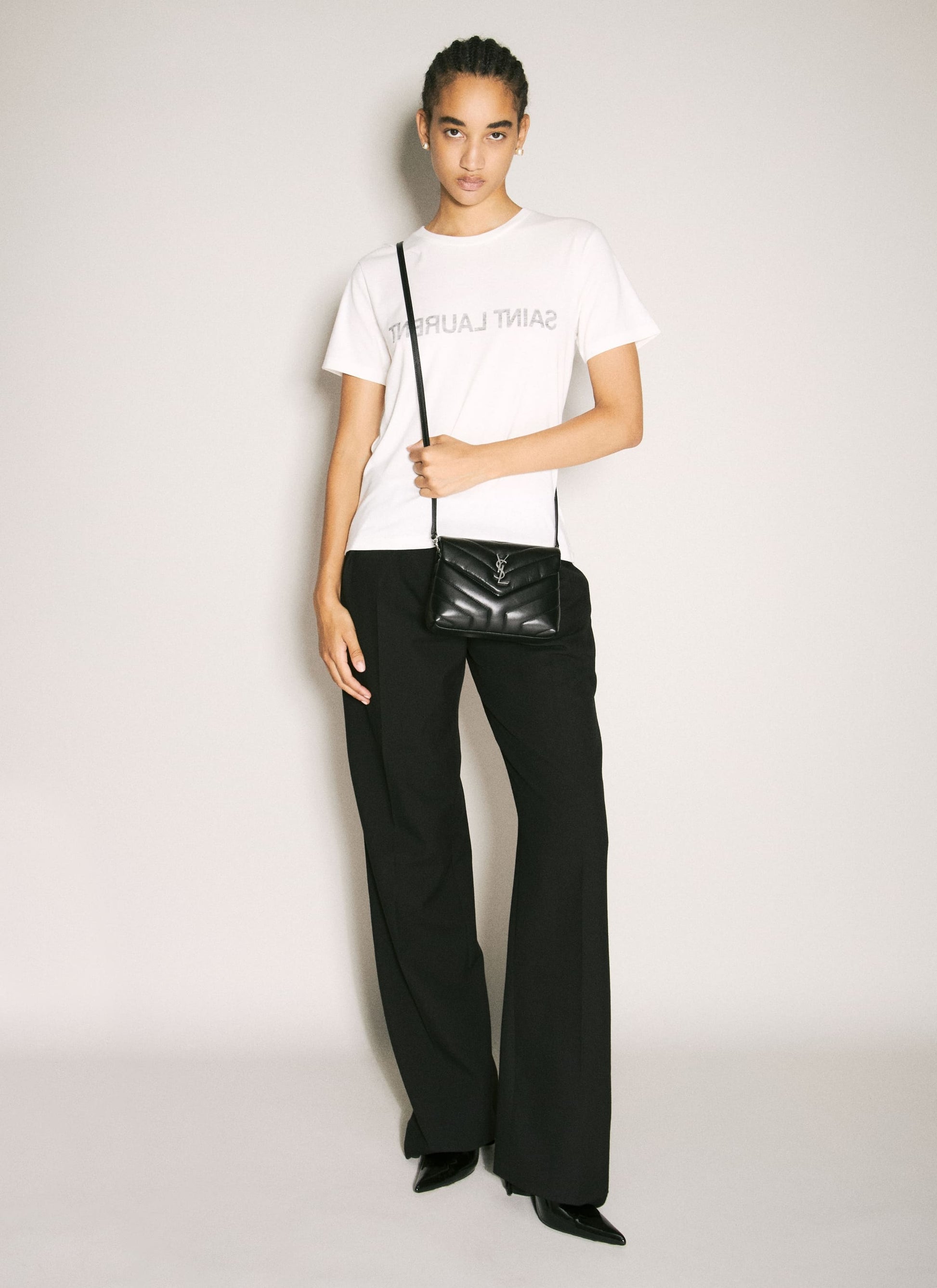 Person wearing a white t-shirt and black pants holding a Saint Laurent Loulou Toy Quilted Leather in Black 678401DV7061000 on a light gray background