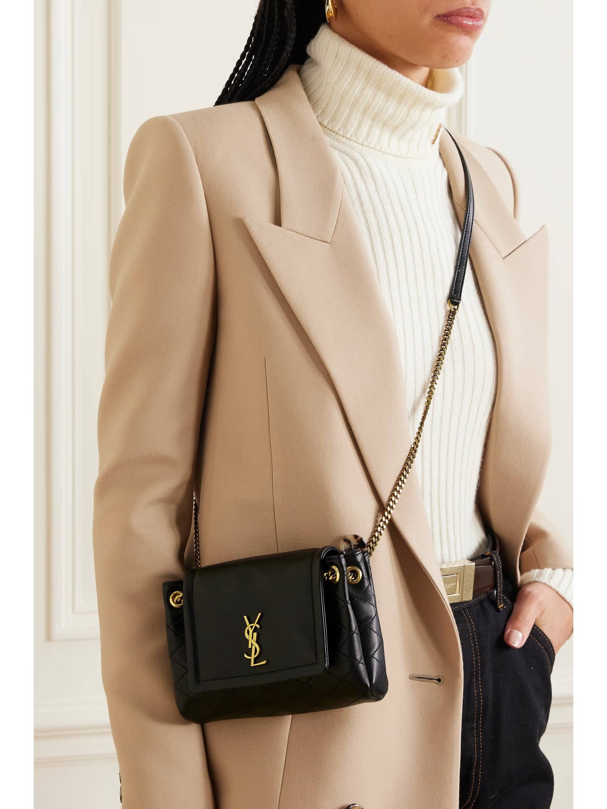 Person wearing a beige blazer and white turtleneck with a Saint Laurent Mini Nolita in Lambskin Black 6727381EL071000