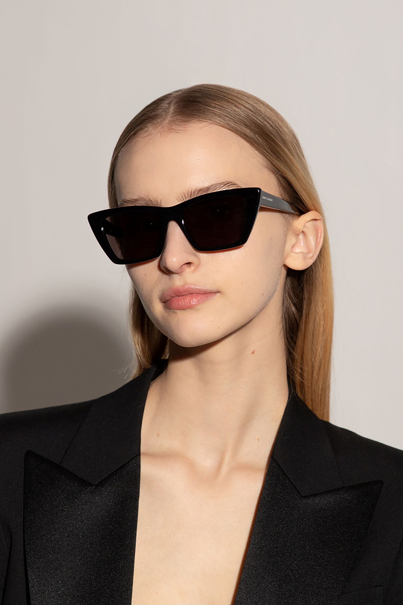 Person wearing black Saint Laurent SL 276 MICA-001 Square Cat-Eye Sunglasses and a black outfit against a plain background