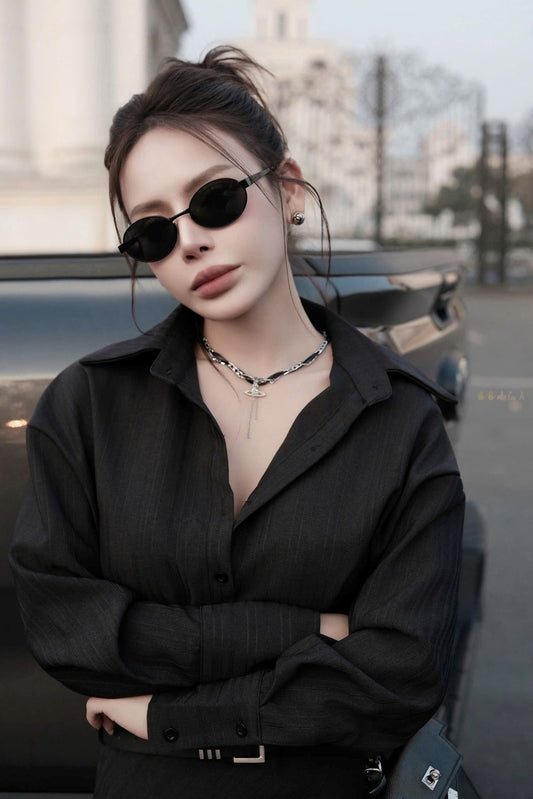 Person wearing Saint Laurent SL 692 001 Oval Sunglasses and a black outfit with a blurred background