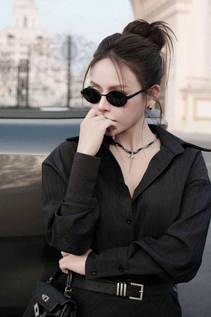 Woman wearing a black outfit with Saint Laurent SL 692 001 Oval Sunglasses and a cityscape background