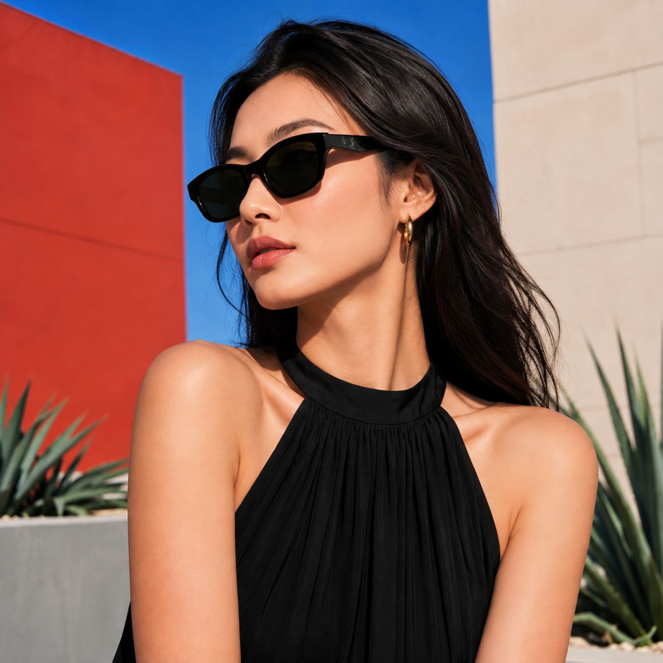 A woman wearingSaint Laurent SL M172 001 Black Rectangular Sunglasses and a black halter top, photographed outdoors against a colorful background with red, blue, and beige walls.