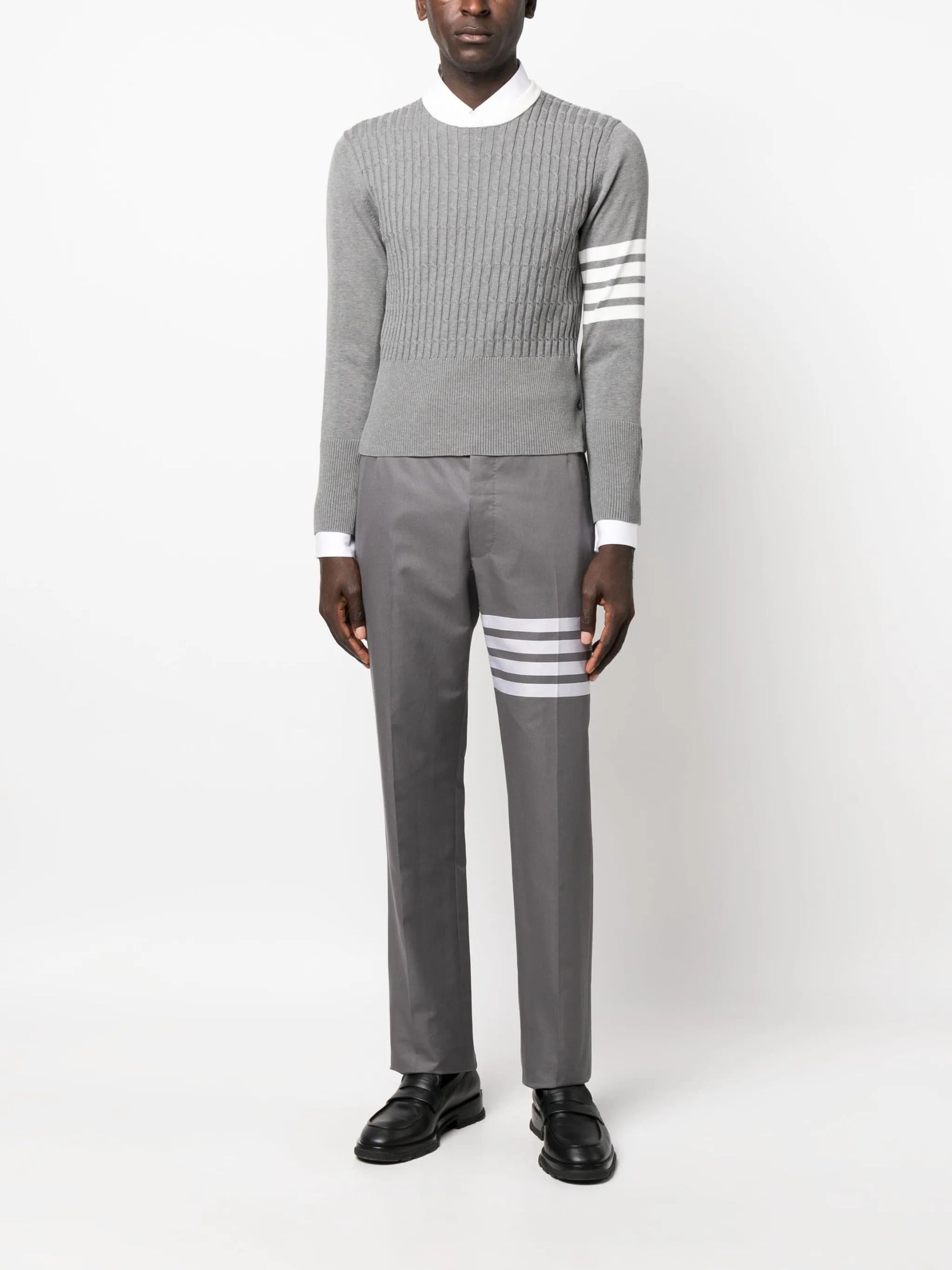 Person wearing aThom Browne 4-Bar Placed Baby Cable Sweatshirt MKA497A Y3014 055 and pants with white stripes on a white background