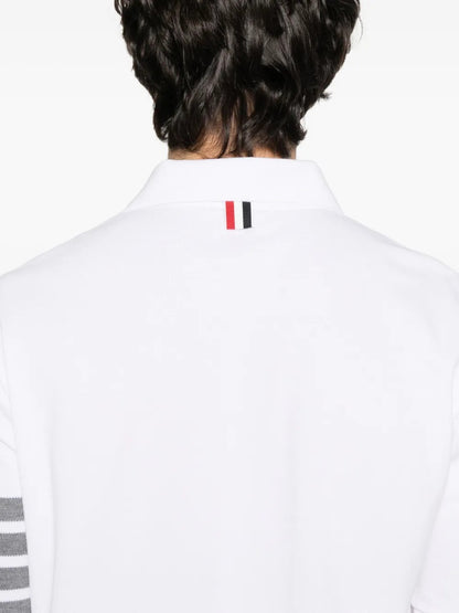 White polo shirt with a brand logo on the collar and stripes on the sleeve, worn by a person.