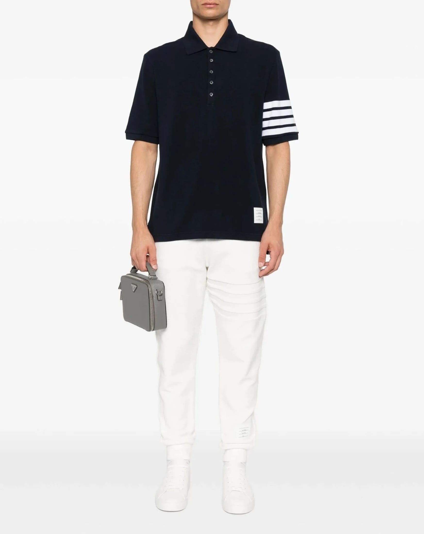 Person wearing a Thom Browne W/ 4-Bar in Sustainable Piqué Navy MJP136G-07976-415 with white stripes and white pants, holding a gray briefcase on a white background.