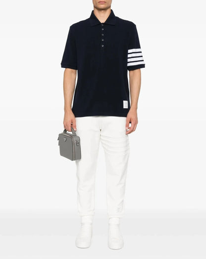 Person wearing a Thom Browne W/ 4-Bar in Sustainable Piqué Navy MJP136G-07976-415 with white stripes and white pants, holding a gray briefcase on a white background.