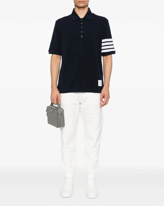 Person wearing a Thom Browne W/ 4-Bar in Sustainable Piqué Navy MJP136G-07976-415 with white stripes and white pants, holding a gray briefcase on a white background.