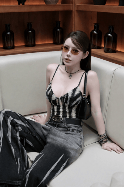 Woman sitting on a white couch wearing a Tiffany TF3104D 617811 Gold Sunglasses, black and white striped top and jeans, with a wooden shelf in the background.