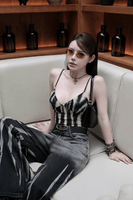 Woman sitting on a white couch wearing a Tiffany TF3104D 617811 Gold Sunglasses, black and white striped top and jeans, with a wooden shelf in the background.