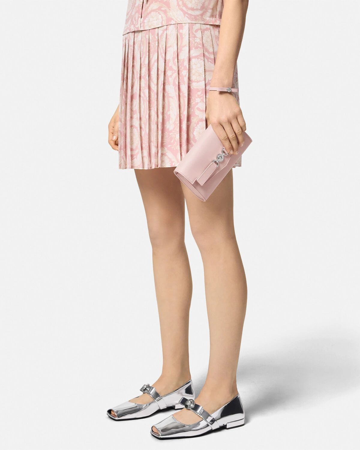 Person wearing a pink pleated skirt and silver shoes with Versace Medusa '95 Crossbody Bag Light Pink 1014319 1A10795 1PT2P on a white background