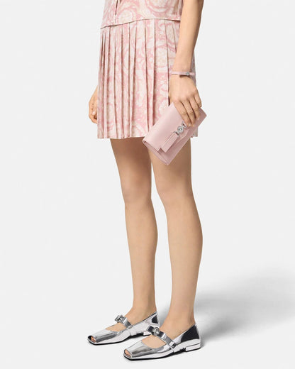 Person wearing a pink pleated skirt and silver shoes with Versace Medusa '95 Crossbody Bag Light Pink 1014319 1A10795 1PT2P on a white background