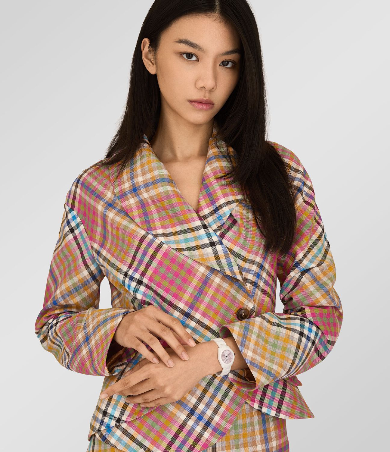 Model wearing a colorful plaid coat with Vivienne Westwood Fenchurch Ceramica Pink White Watch vv358lpkwh 8050164232122 on a plain background