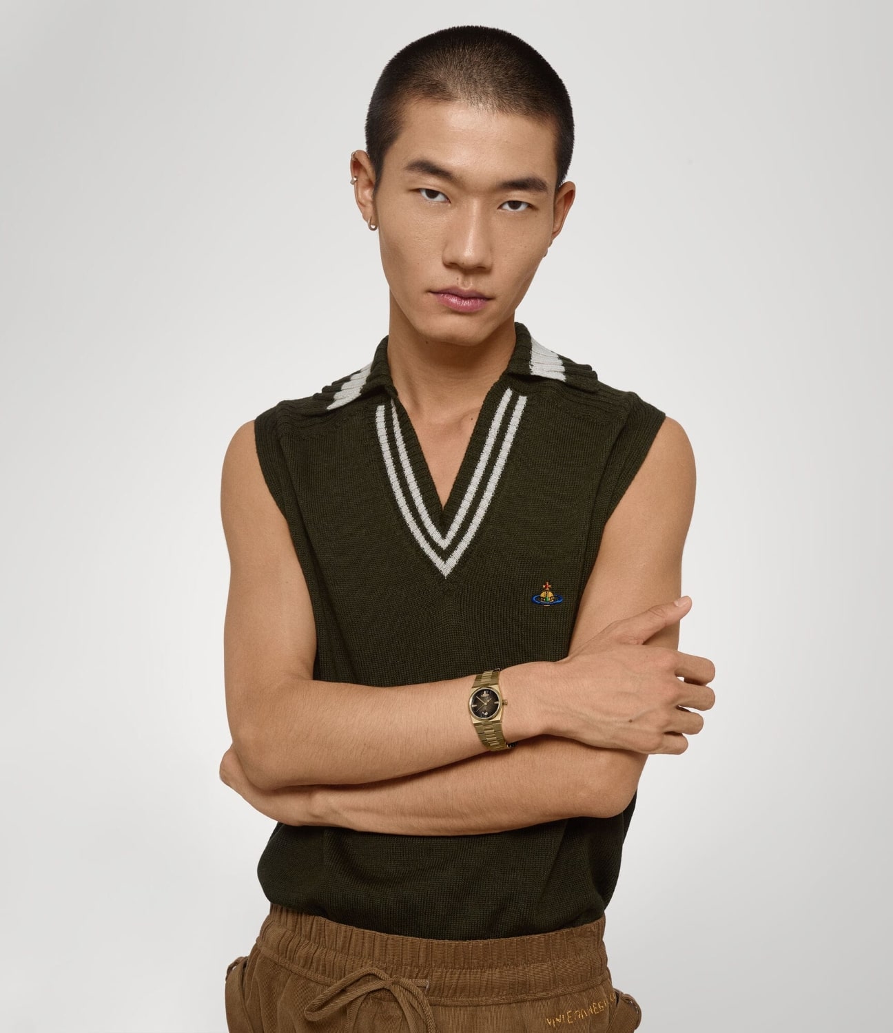 Man wearing a dark green sleeveless sweater with a Vivienne Westwood Hoxton Black Dial Gold Watch VV332MTGD 8050164231873 against a plain background