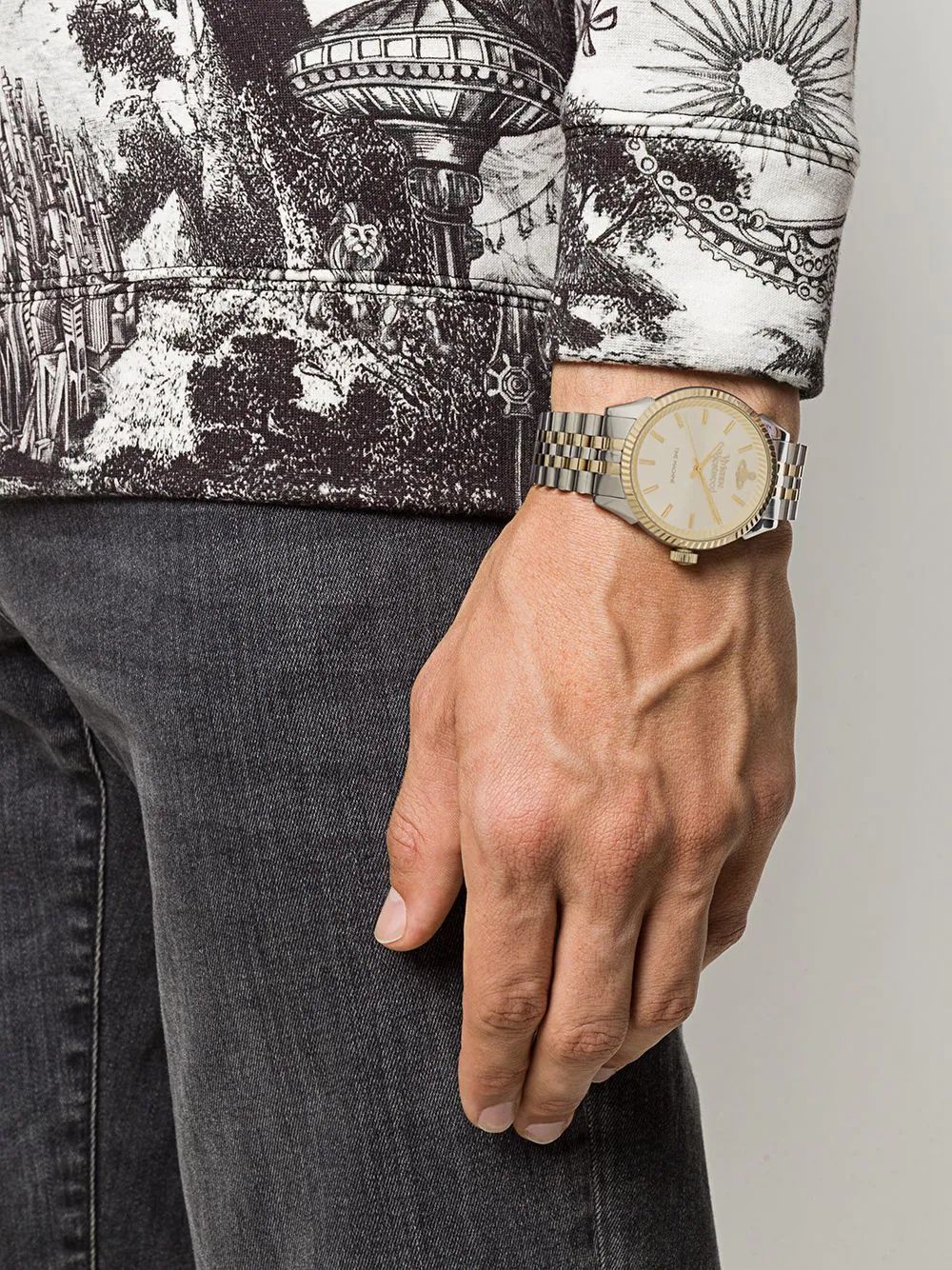 Hand wearing a Vivienne Westwood Seymour Homme Champagne Dial Silver Watch VV242CMSG with a detailed patterned shirt and jeans on a neutral background