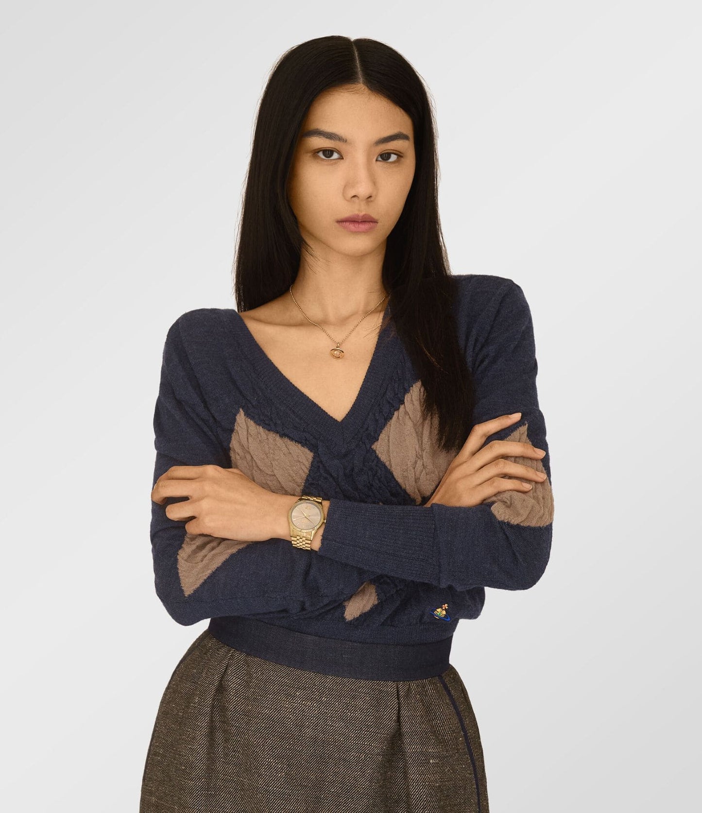 Woman wearing Vivienne Westwood Seymour Rose Dial Gold Watch vv240pkgd in a navy sweater with brown diamond patterns on a light gray background