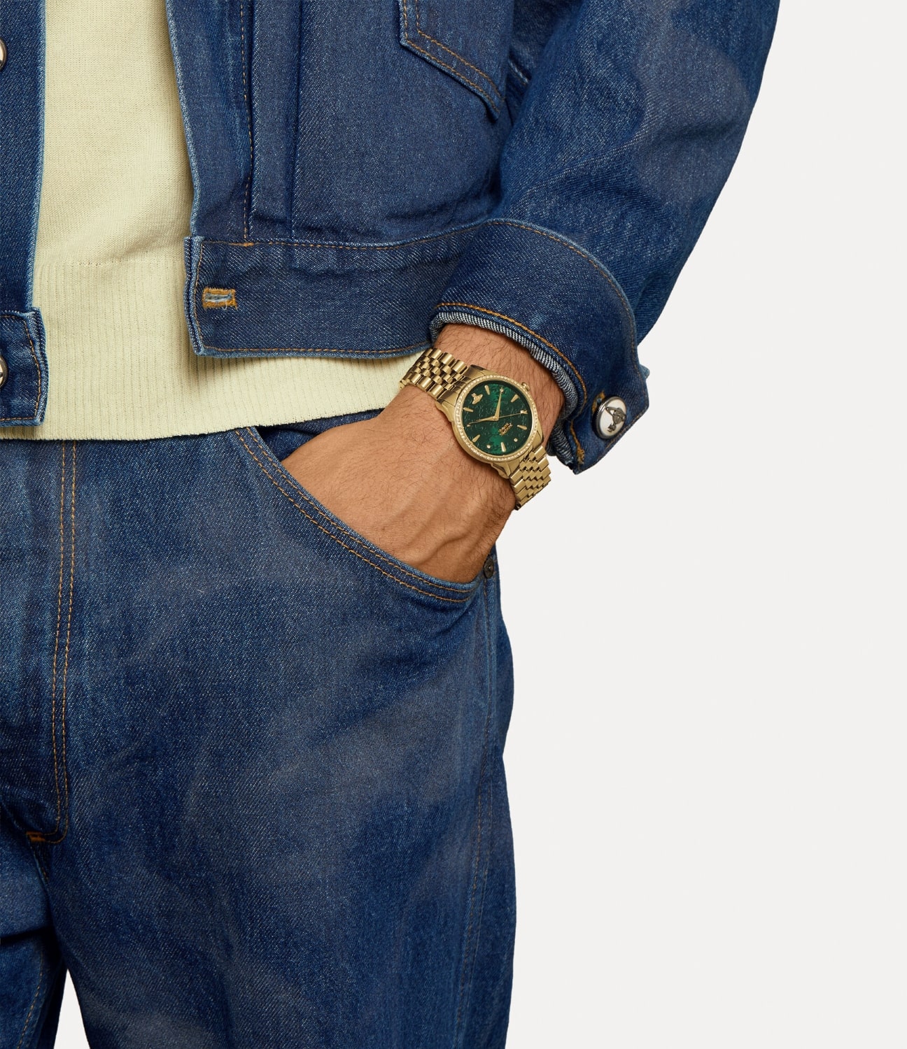 Person wearing a Vivienne Westwood Wallace Green Dial Gold Watch VV208GDGD 8050568621317 with a green face, dressed in blue jeans and a denim jacket.
