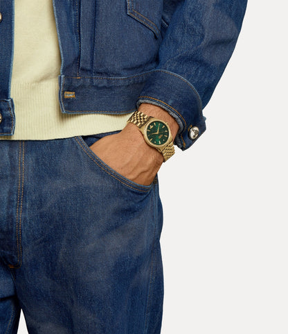Person wearing a Vivienne Westwood Wallace Green Dial Gold Watch VV208GDGD 8050568621317 with a green face, dressed in blue jeans and a denim jacket.
